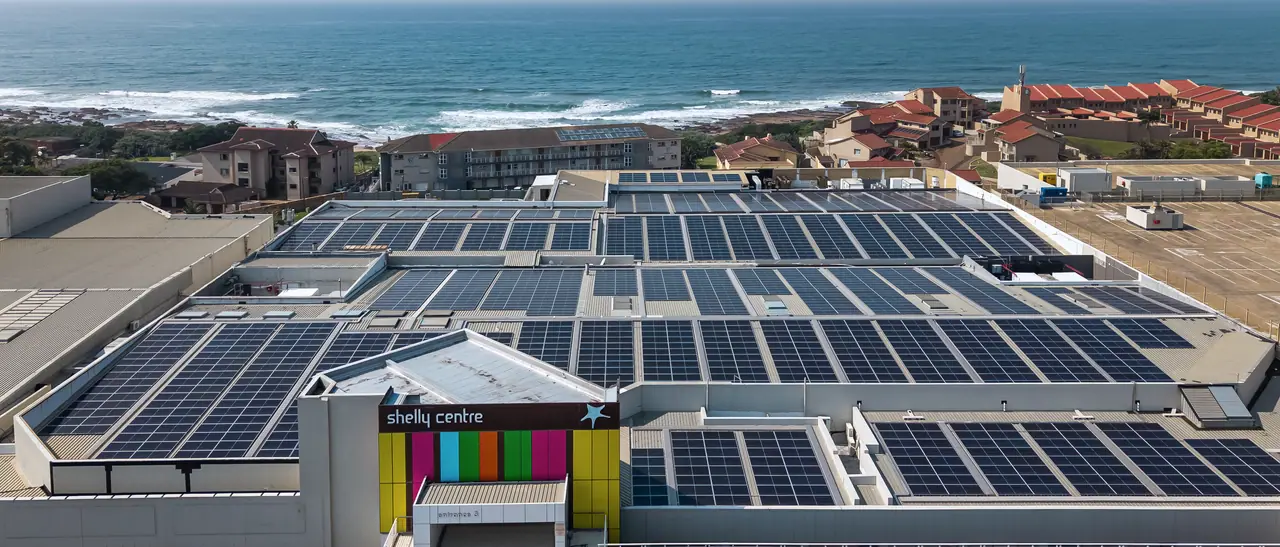 Aerial view of Shelly Centre, its roofs covered in rows of solar modules, with the coast and the sea beyond