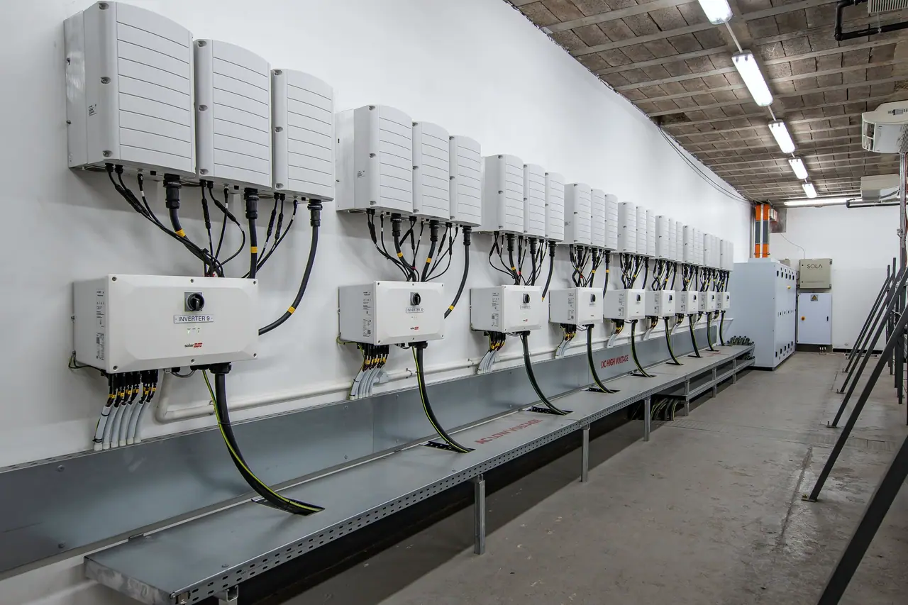 A long inverter room at Belgotex, a row of wall-mounted inverters above a cable tray